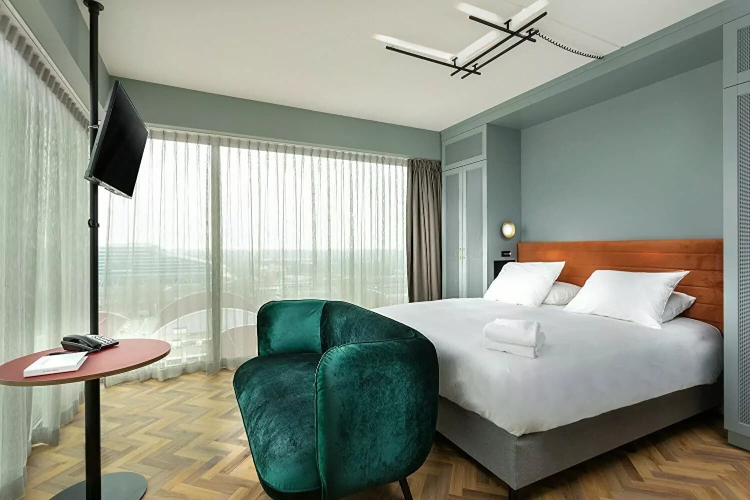 Olympic Hotel room with a double bed, green chair, and panoramic windows